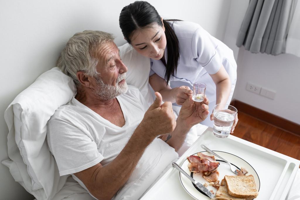 Nurse give pill to senior man after breakfast 